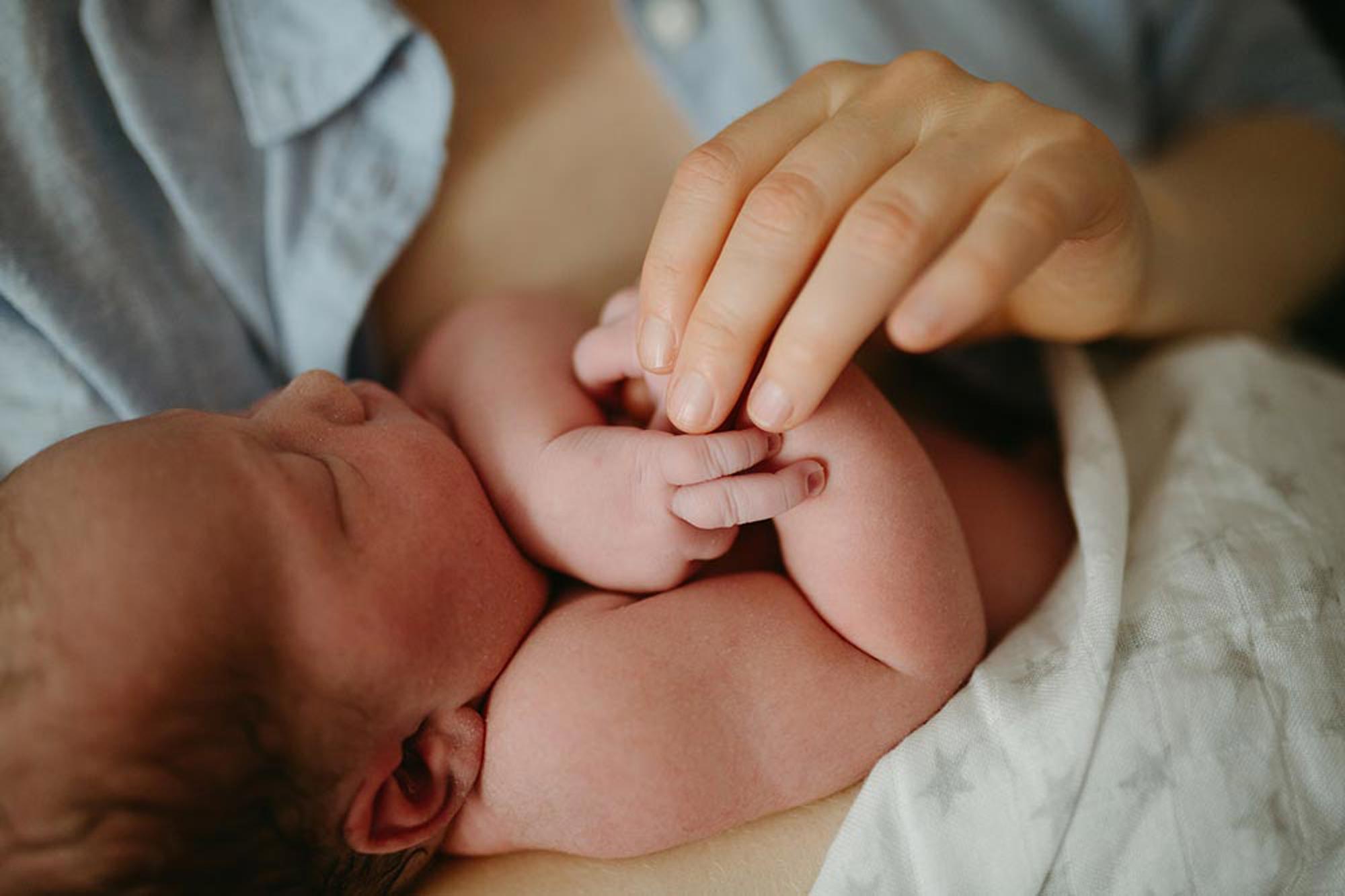 Förälder myser och håller i sin bebis hand
