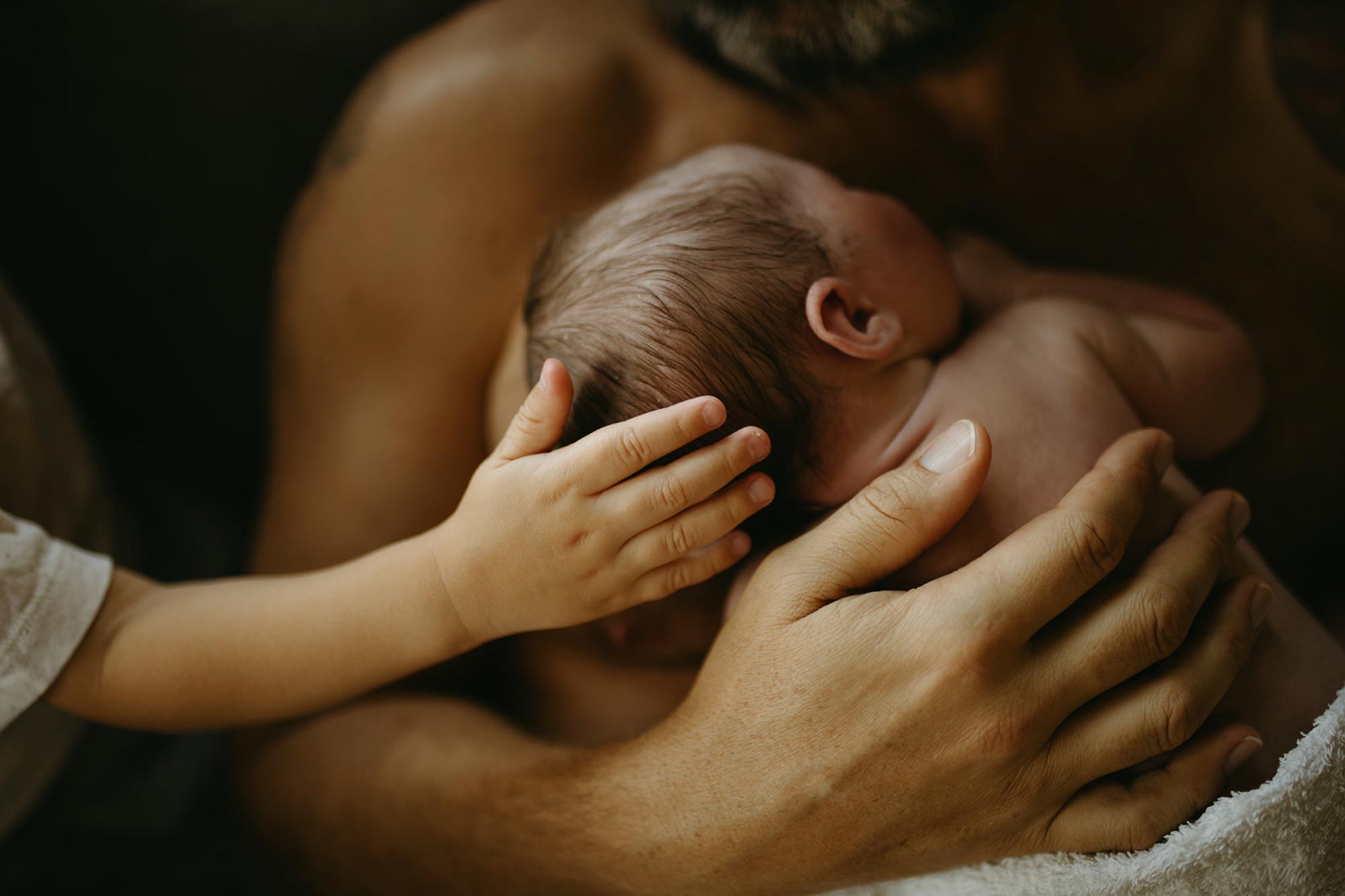 Förälder håller om sitt nyfödda barn medan äldre syskon håller sin hand mot sitt nyfödda syskons huvud