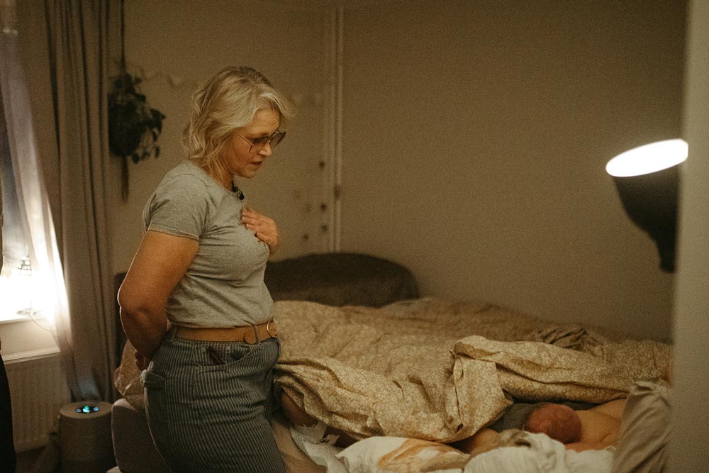 Johanna håller sin hand mot sin bröstkorg och pratar med den nyblivna mamman som ligger i en säng