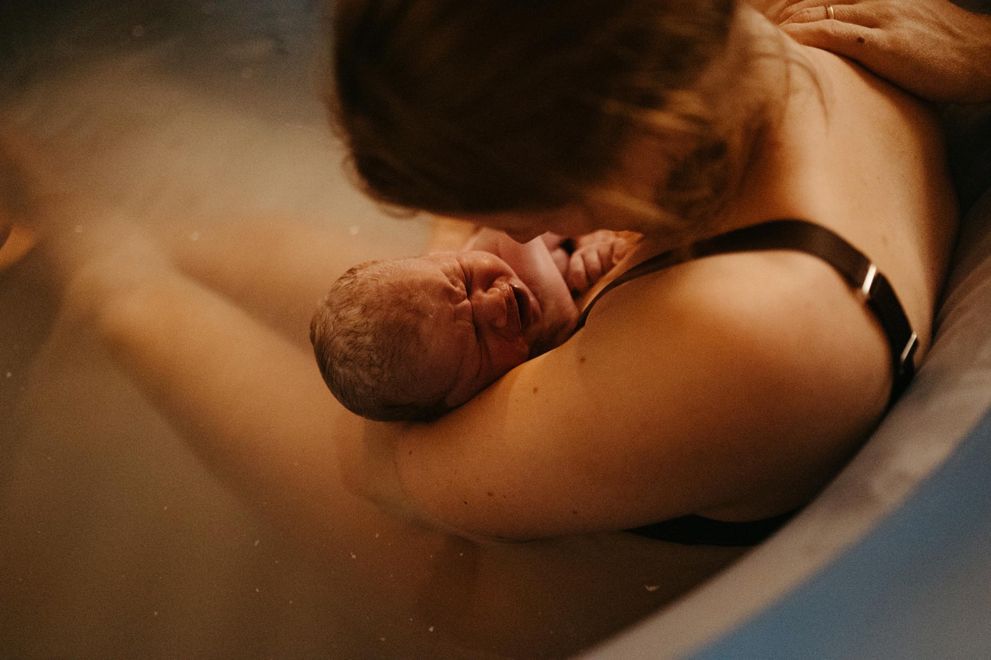 Mamma som sitter i en födselpool håller om sin nyfödda bebis