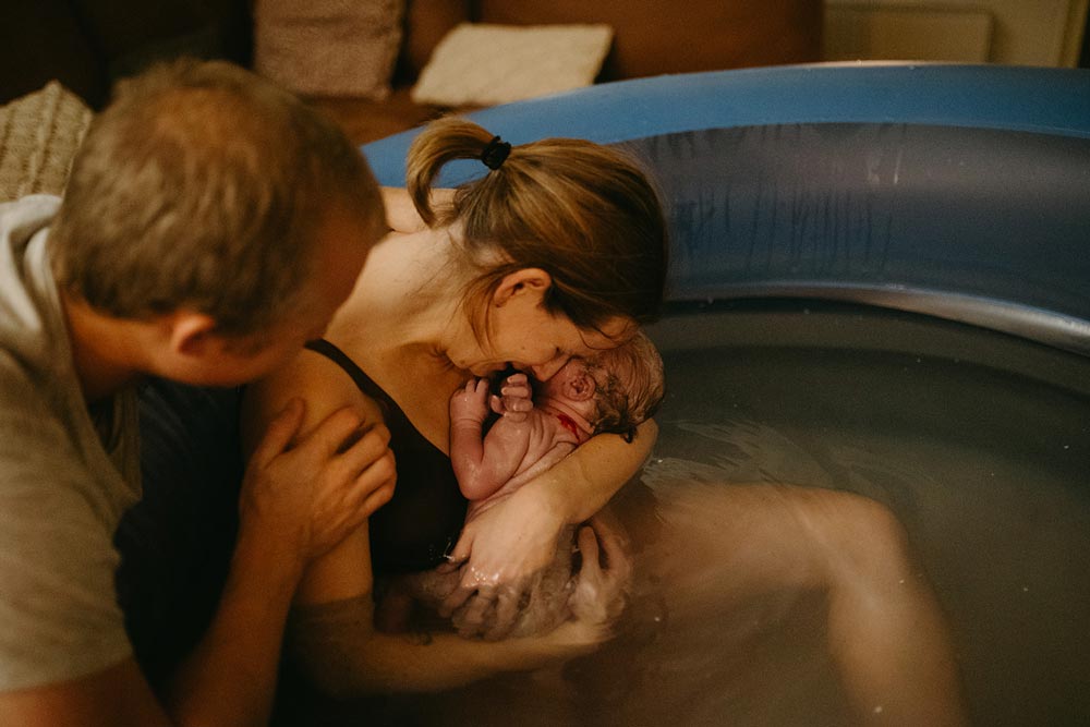 Förälder håller nyfödd i famnen, partner stödjer och håller om mamman