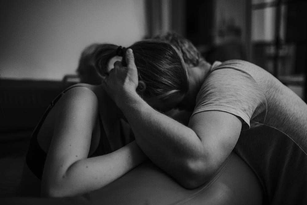 Partner håller om den födande i födselpool under födsel