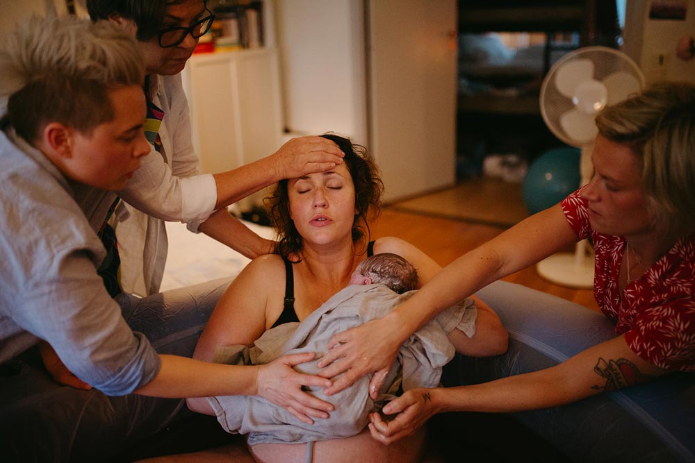 Partner samt nära och kära visar stöd till mamma som håller sitt nyfödda barn i en födselpool