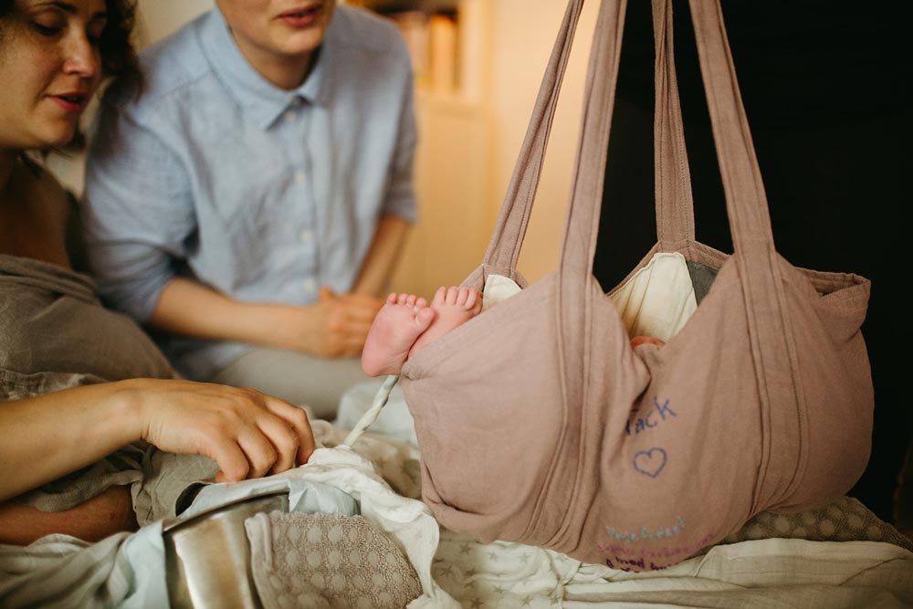 Nyfödd barn vägs i en tygpåse medan föräldrarna tittar på
